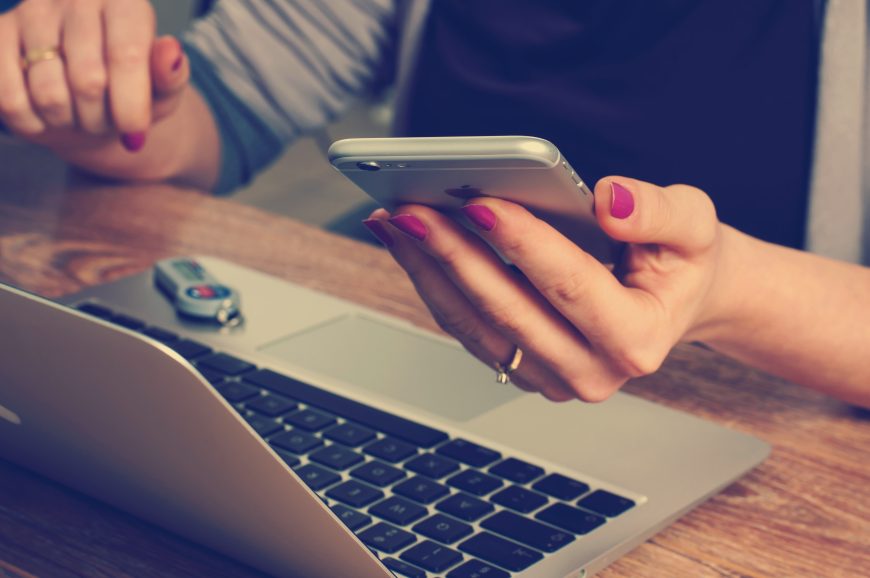 woman holding a phone and a working on a laptop.